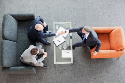 businessmen shaking hands across coffee table